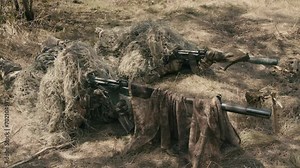 A close-up of a sniper wearing a camouflage suit or grass cloak, waiting and looking through a rifle scope. The sniper aims and shoots. Marksmanship shooting. Cinematic shot Stock Video
