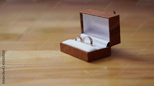 Wedding engagement rings in a brown box lie on a wooden background. Video shot by dolly cart.