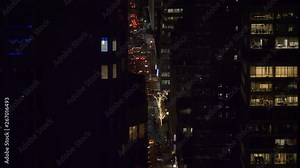 Spectacular view of night time traffic moving through the buzzing streets of New York. Workers in corporate offices stay up late to extend their workday in busy metropolitan city. Bright lights of NYC