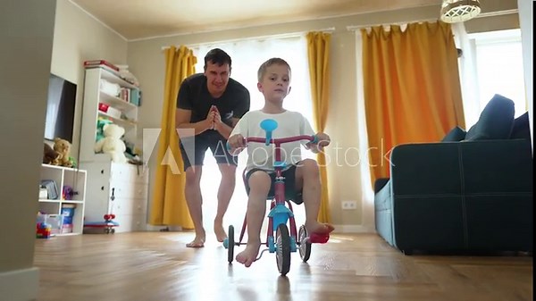 Father encouraging child on tricycle. boy riding tricycle indoors. playtime with father. Child learning to ride tricycle. Father and son bonding. child on tricycle at home. moments with father child.