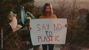 Young woman activist with glued mouth holding encouraging white poster Say no to plastic standing at landfill site with garbage nature environmental community earth eco environment outdoor slow motion