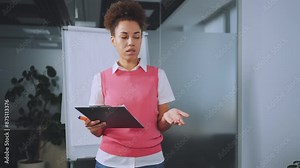 Group of coworkers participating in voting session during office meeting. Female leader stands with clipboard while team members raise hands to vote. Concept of teamwork and decision-making