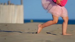 Lowangled Shooting of Legs of a Little Girl in Pink Running on the Beach