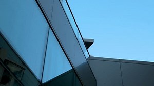 Modern architectural detail with angled glass facade against sky.