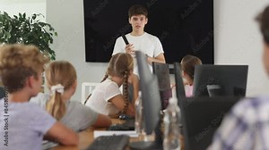 Young guy teacher teaches group of children students to work with computer in lesson