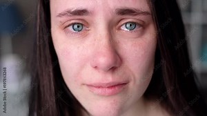 Young woman crying looking at the camera in slow motion. Tears comes out of an eyes
