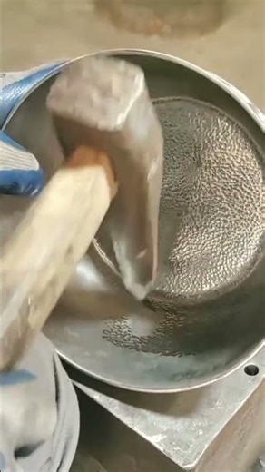 Hammering a metal bowl to create a textured surface using a specialized rounded metal hand tool