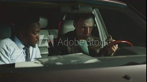 Through windshield shot of two multiethnic police detectives having coffee with donuts, discussing suspect profile while tracing him in car at night