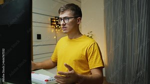 Young Man in Yellow T-Shirt and Eyeglasses at Computer, Confused by Display, Trying to Resolve the Situation by Typing.