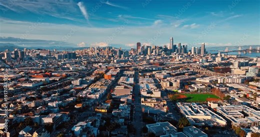 Dense urban landscape of San Francisco lit by the setting sun. Drone footage approaching the gorgeous downtown of the city with high-rise architecture.