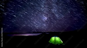 Time lapse of Star trails in the night sky over mountains and glowing tent. 4K
