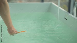 Woman leans over bathtub, holding orange thermometer to ensure safe bathing conditions for her baby. Scene captures careful preparation by mother. Concept of nurturing childcare, loving maternal care