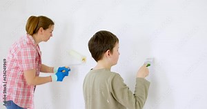 Happy family mother and son paint the wall with paint using roller and brush