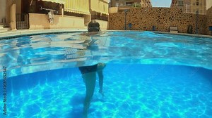 Underwater swimmers performing synchronized leg movements, navigating swimming pool while wearing swimsuit and protective goggles.Two teenagers in swimming pool