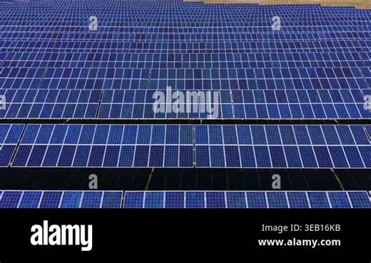 Solar panels are arranged in neat rows across a large field under bright sunlight. There are no obstacles blocking the sun's rays. The sky is clear and blue Stock Video Footage - Alamy
