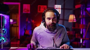Esports player films himself playing videogames in front of internet fans during livestream, providing engaging commentary while battling foes. Zoom out shot of pro gamer streaming gaming session