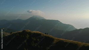 Happy young couple hiking on mountain top in the alps mountains on panoramic Monte Baldo at Garda Lake and Verona in Italy, Valpolicella wine and vinery area, circling around by drone as aerial view.