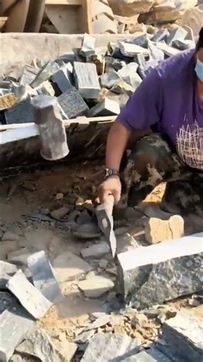 splitting large stone blocks manually into smaller pieces using a heavy hammer and metal chisel