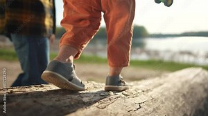 baby toddler plays in a forest park. close-up of a child feet walking along a log of a fallen tree. happy family child dream concept. child in sneakers walks on a fallen tree in a park lifestyle