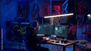 Hacker in underground warehouse writing lines of code on computer screen to make malware that get past security systems. Man in hidden HQ building scripts that can hack devices, dolly in shot