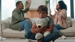 Sad little child boy hug teddy toy while mom dad fighting screaming arguing upset kid son suffer feel lonely parents conflict divorce fight psychological trauma problem custody in multiracial family