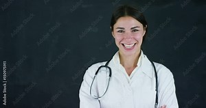 Portrait of a beautiful female doctor (student) stands by a black board, on a black background. Concept: ideas, school, university, chemistry, science, teachers, memory, biology, physician, college.