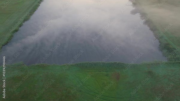 Drone captures mist over foggy pond at dusk, tendrils of fog intertwining with open land creating a mystical effect in the farmland