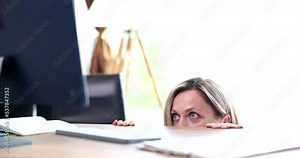 Shocked woman looks at computer screen from under table and eyes widen in horror