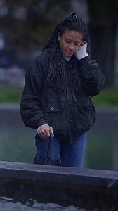 A contemplative woman stands by the fountain enjoying the rainy weather around her
