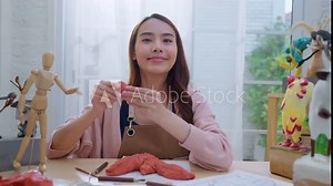 Asian Female artist an clay sculpture, live streaming online tutorial for her followers and explain them how to properly define theshape anatomy, while making the monster clay statue at home studio Stock Video