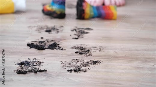 Muddy footprints on the surface clean floor in the living room. The boots are wet from outdoor play, and the room shows signs of recent rain activity. Home care and cleaning service.