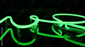 A close shot of a detail of a green neon sign. green neon lights close up. Light sign, green neon sign turning on and off in a dark room in a neon sign store. Close up. horizontal orientation video