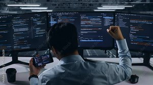 Back View Of Happy Asian Man Developer Looking At Code On Mobile Phone While Write Code With Multiple Computer Screens In Data Center Stock Video