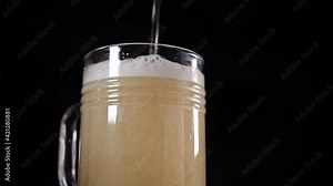 Glass beer mug. Non-alcoholic beer, low key, dark. Beer is poured into the mug with a thin stream