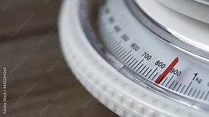 Mechanical kitchen scale with dial. A white kitchen scale on a wooden table measures 900 grams. Close-up.