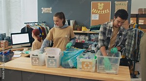 Long shot of group of volunteers sorting rubbish for recycling and preparing second-hand clothes while working in donation centre for people in need