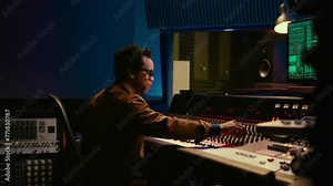 Music producer operating mixing console in control room and working with audio recording software on pc, post production. Sound engineer editing tracks to produce new songs. Camera B.