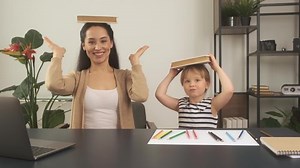 Little girl studying with mother or teacher at study table with laptop computer, books and having fun learning. Holding book on their heads