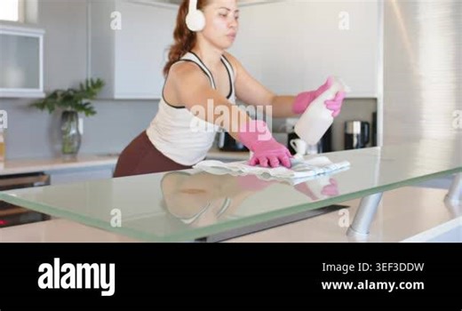African American woman cleaning glass bar in kitchen lifting spray bottle, wiping to remove streaks. Countertop, sleek, home, gloves, headphones, buff, cloth Stock Video Footage - Alamy