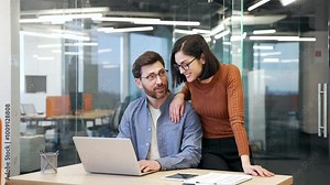 Young female employee flirts with a coworker at workplace in business office. Attractive beautiful woman puts her hand on shoulders of a colleague, smiles, jokes, starts a romance with a businessman Stock Video