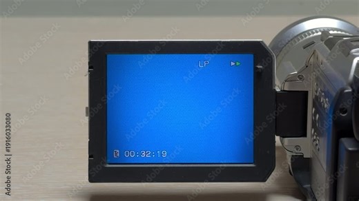 A vintage camcorder begins fast-forwarding through a tape. The internal gears spin rapidly, producing an anxious, high-pitched mechanical whir. This sharp sound echoes as the timestamp advances.