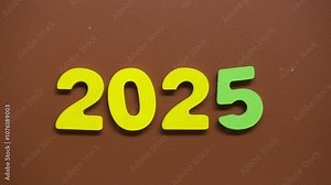 Stop motion sequence showing the colorful numbers "2025," with yellow and green digits arranged on a brown textured background. Perfect for projects celebrating the upcoming year, New Year’s themes