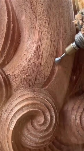 carving detailed brown patterns on a wood surface using a small electric hand rotary power tool