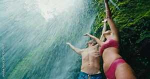 Attractive adventurous young couple relaxing under beautiful waterfall
