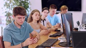 Serious focused young student studying together with coursemates in computer workshop, actively using smartphone to access online learning materials. High quality 4k footage