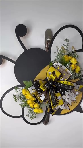 Brighten up your entryway with this charming bumblebee-shaped door hanger bursting with summer cheer! Handcrafted on a wooden bee cutout, this adorable piece features lush yellow florals, lifelike greenery, and a layered designer bow with buzzing bee prints, polka dots, and bold ribbon patterns. Perfect for spring and summer decorating, this bee hanger adds a playful pop of color to your front door, porch, sunroom, or even your bee-themed kitchen. It’s a great alternative to a traditional wreath