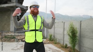 Happy engineer contractor dancing on construction site in good mood, crazy bearded worker, calls you to dance.