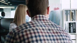 Free stock video - Caucasian female doctor wearing medical mask sitting at desk explaining coronavirus lung disease to male patient in medical consultation