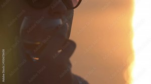 Slow motion close-up clip of a woman in sunglasses with a beauty spot on cheek drinking pure water from a glass. Nice scene with sea and sunset in background