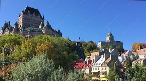 The iconic Chateau Frontenac, and hilltop area including the Louis St. Laurent building and the charming Petit Champlain district with colorful buildings below. Canadian flags waving, blue sky.
